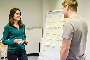 Studentin und Student vor einem Flipchart, auf dem Post-its geklebt sind